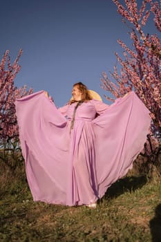 Woman blooming peach orchard. Against the backdrop of a picturesque peach orchard, a woman in a long pink dress and hat enjoys a peaceful walk in the park, surrounded by the beauty of nature