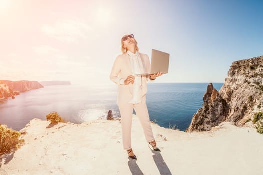 Digital nomad, Business woman working on laptop by the sea. Pretty lady typing on computer by the sea at sunset, makes a business transaction online from a distance. Freelance remote work on vacation