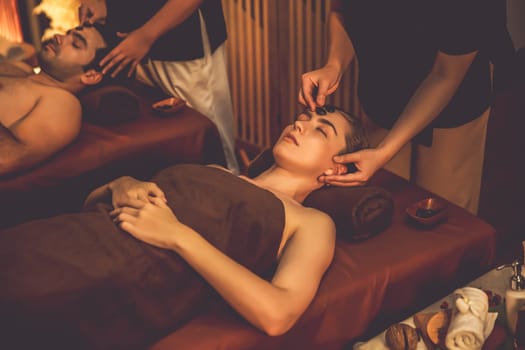 Couple customer enjoying relaxing anti-stress head massage and pampering facial beauty skin recreation leisure in warm candle lighting ambient salon spa in luxury resort or hotel. Quiescent