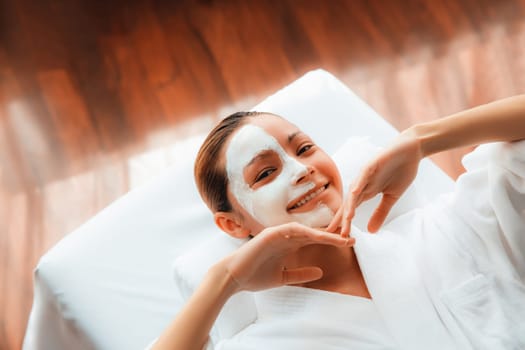 Serene daylight ambiance of spa salon, top view woman lying on massage table smiling and rejuvenating with face cream spa massage. Facial skin spa treatment and beauty care concept. Quiescent