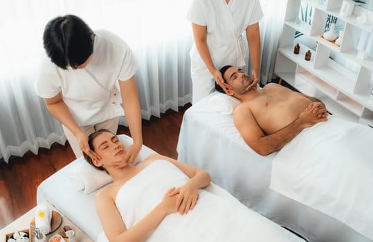 Caucasian couple enjoying relaxing anti-stress head massage and pampering facial beauty skin recreation leisure in dayspa modern light ambient at luxury resort or hotel spa salon. Quiescent