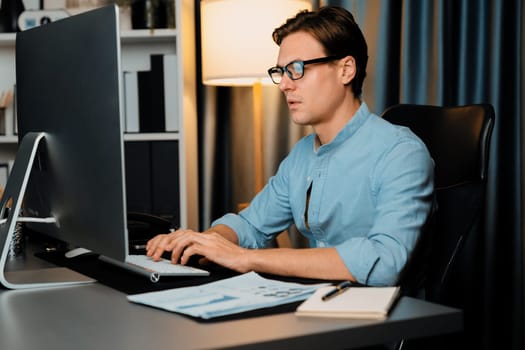Smart businessman analyzing business paragraph dynamic database marketing analysis plan surrounded paper sheet and pc monitor report to compare with document data at home office at night. Pecuniary.
