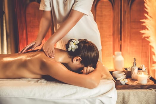 Caucasian woman customer enjoying relaxing anti-stress spa massage and pampering with beauty skin recreation leisure in warm candle lighting ambient salon spa at luxury resort or hotel. Quiescent