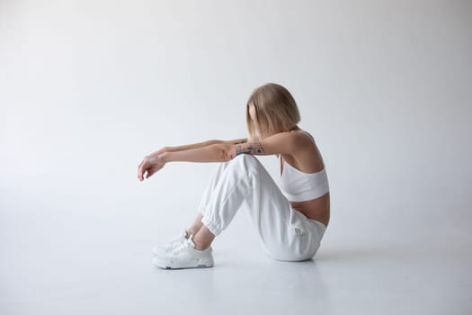 Beautiful blonde girl in a white top and tights posing on a white background. High quality photo