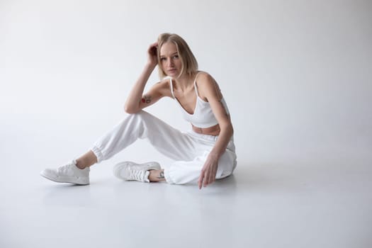 Beautiful blonde girl in a white top and tights posing on a white background. High quality photo