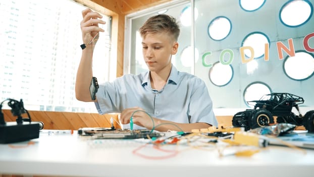Smart happy boy inspect or learning to use electronic tool to fix car model. Highschool student studying about electric equipment to repair robotic machines while sitting at STEM class. Edification.