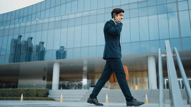 Smart business man using phone to talking while walking at building. Happy manager walking at street while talking on smart phone to discuss business plan or marketing strategy or working. Exultant.