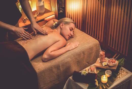 Woman customer having exfoliation treatment in luxury spa salon with warmth candle light ambient. Salt scrub beauty treatment in Health spa body scrub. Quiescent