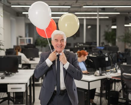 Portrait of a cheerful mature business man holding balloons in the office