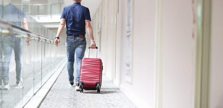 Rear view of man pulling suitcase down hotel corridor. Rest at hotel concept