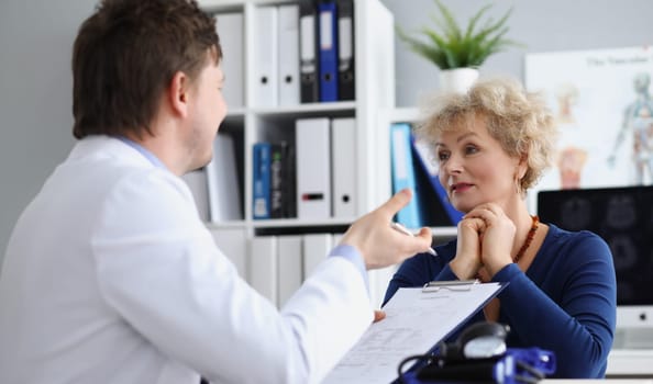 Elderly woman sitting at table at doctor appointment in clinic. Insurance medical care concept