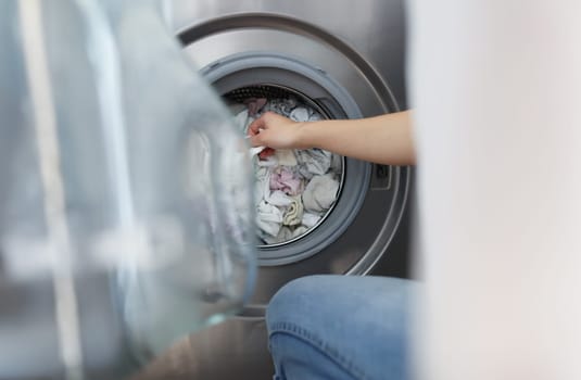 Woman pulling out clean clothes from washing machine in bathroom closeup. Repair and maintenance of household appliances concept
