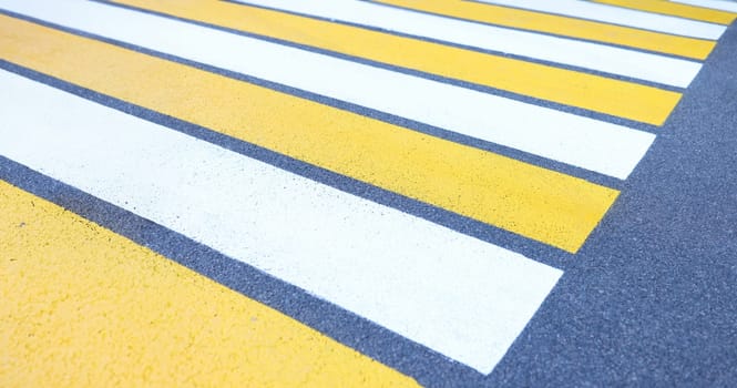 Closeup of white and yellow stripes on gray asphalt background. Crosswalk concept