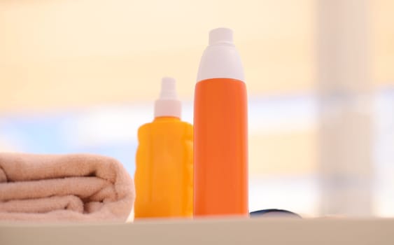 Two orange bottles with sunscreen lying on beach near towels closeup. Skin protection during summer season concept