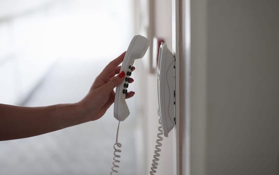 Woman hand picking up phone in hotel corridor closeup. Hotel room service concept