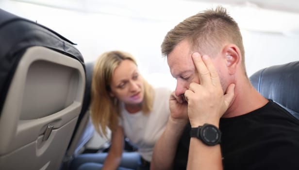 Young man is flying in airplane and holding sore head. Aerophobia fear of heights concept