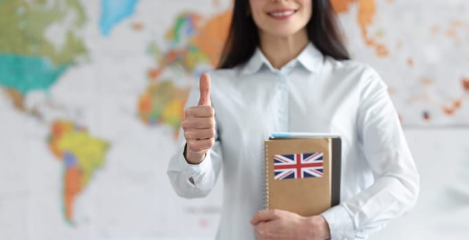 Woman holding english textbooks on background of world map and showing thumb up closeup. English lessons concept