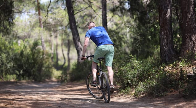 Young man riding bicycle along path of park back view. Outdoor cycling concept