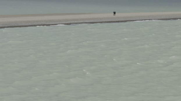 Couple walks on slim beach between icy waters, caught in slow-motion.