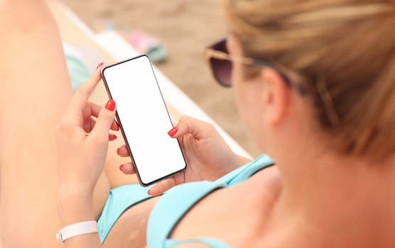 Young woman sitting on beach lounger and holding mobile phone in her hands closeup. Remote communication concept