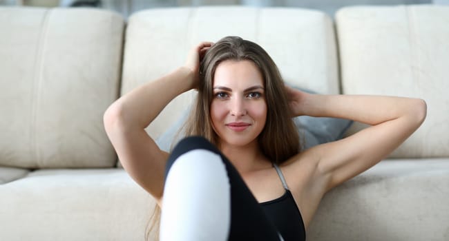 Girl lies with her hands behind her head, exercise. Young woman does exercises to strengthen abs, lying on her back. Kalanetik at home. Athlete is in good mood. Achievement sports results.