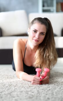 Girl in sportswear holds dumbbell in her hands. Model pays close attention to development hands. Exercise for muscles shoulders and arms. Woman is resting from fitness with dumbbells.
