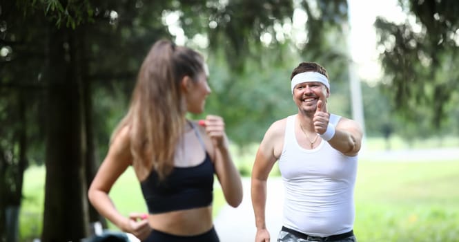 Man in park shows ok gesture to sports girl. Running has beneficial effect on respiratory system body. Happy girl looks at man who smiles at her. Classes relieves stress and uplifting.