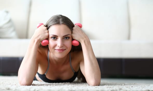 Girl learns to correctly perform exercises at home. Exercises with dumbbells give good load on all muscles. Beginner training with small weight. Girl resting lying on floor and holds dumbbells