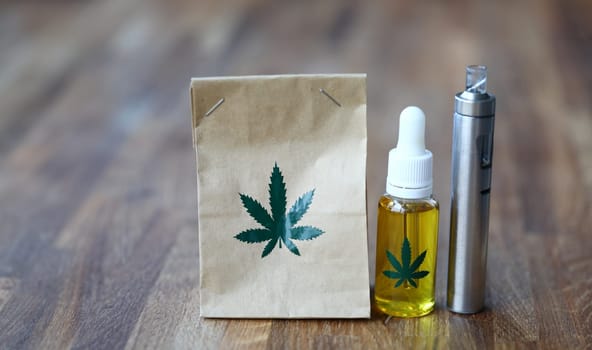 Paper organic bag with marijuana vaporizer cbd oil stand on a wooden table closeup