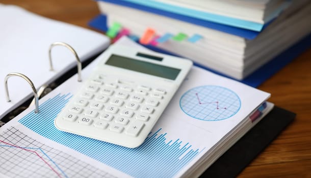 White caculator with business chart lie on the office table background closeup. Financial education concept