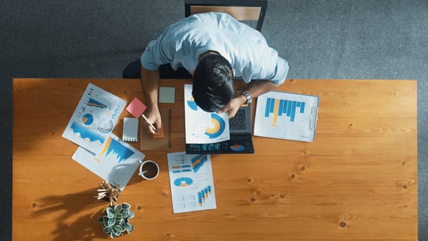 Top aerial view of manager working on laptop while looking at data analysis. Leader compare financial statistic graph while making decision at meeting table with document scatter around. Convocation.