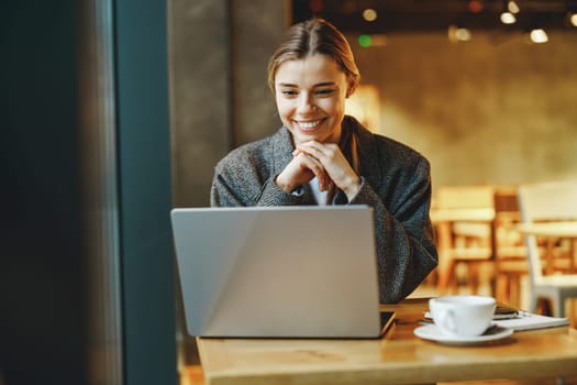 Pretty young female freelancer working on laptop while sitting in cozy cafe