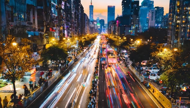 A busy city street with lots of traffic and people. The lights from the cars and street lamps create a bright and lively atmosphere