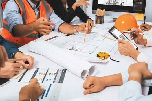 Diverse group of civil engineer and client working together on architectural project, reviewing construction plan and building blueprint at meeting table. Prudent