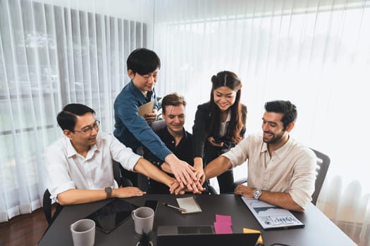 Group of diverse office worker join hand together in office room symbolize business synergy and strong productive teamwork in workplace. Cooperation and unity between business employee. Prudent