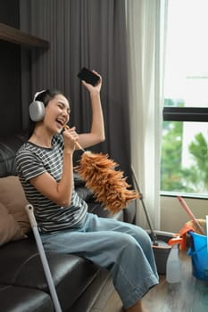 Overjoyed young housewife in headphones singing while cleaning living room.