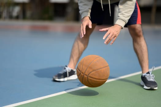 Cropped shot of sporty man bouncing ball in an urban court. Sport and active lifestyle concept.