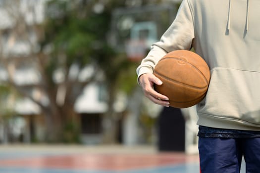 Teenage man holding a ball standing on the basketball court. Sport and active lifestyle concept.