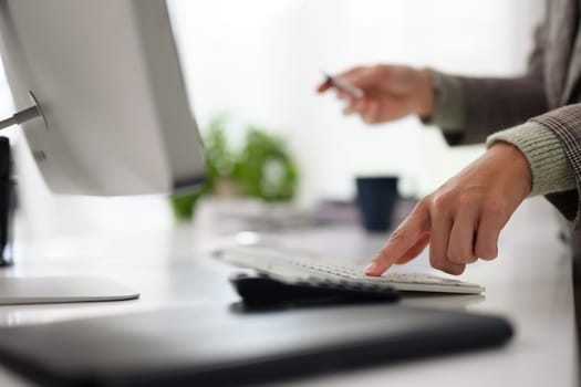 Closeup woman holding a credit card and calculating expenses at office desk.