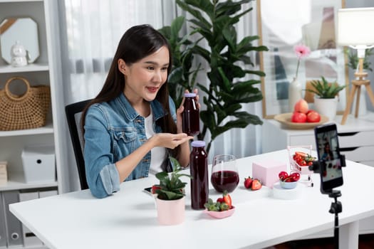 Smiling young beautiful Asian reviewing tasty mixed strawberry and cherry juice detox drinks, showing healthy product to promote for special promotion selling on social media online record. Stratagem.