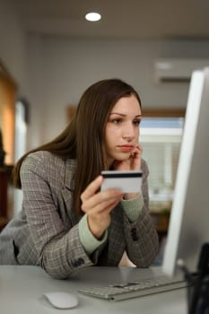 Businesswoman holding a credit card and looking at computer, having problem with payment.