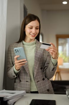 Portrait of smiling businesswoman with credit card doing online shopping on mobile phone.