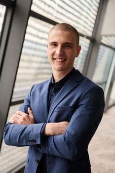 A young businessman exudes confidence and authority as he stands with crossed arms in the heart of his bustling factory, symbolizing leadership and success in the industrial world