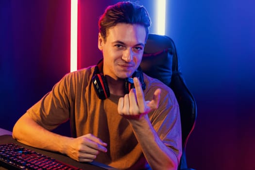 Host channel of gaming smart smiling streamer looking at camera pose gesture, live steaming on social media online in cyber gamer team skill players group at neon blue and pink light room. Pecuniary.