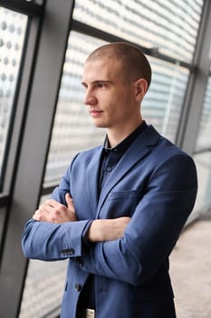 A young businessman exudes confidence and authority as he stands with crossed arms in the heart of his bustling factory, symbolizing leadership and success in the industrial world