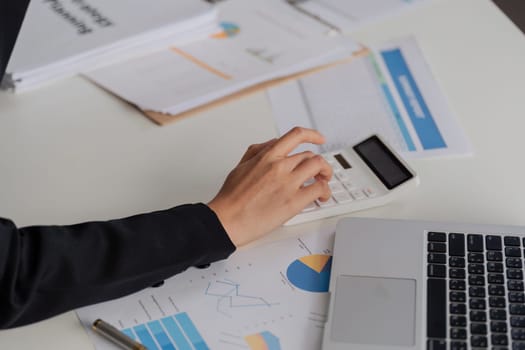 A woman is using a calculator on a desk with papers and a cell phone. The scene suggests a busy work environment where the woman is focused on her tasks