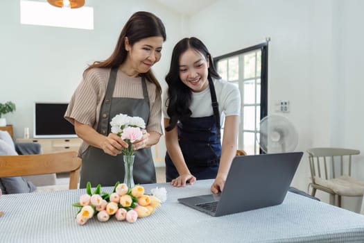 mother and daughter arrange flowers together as a hobby. mother and daughter spend free time doing flower arranging activities together and looking at laptop.