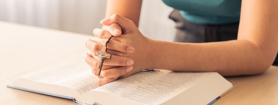 Cropped image of female reading a bible book while holding cross at wooden table with blurring background. Concept of hope, religion, faith, christianity and god blessing. Warm. Burgeoning.