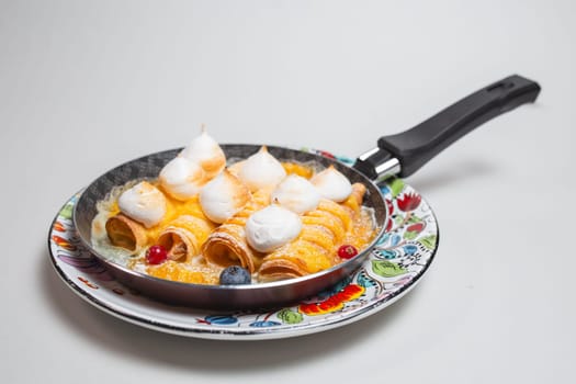 Pancakes with meringue and berries in a frying pan on a white background.