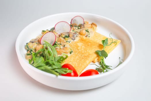 Savory crepe with creamy mushroom sauce, fresh greens on a white plate. Perfect for a light and satisfying meal.